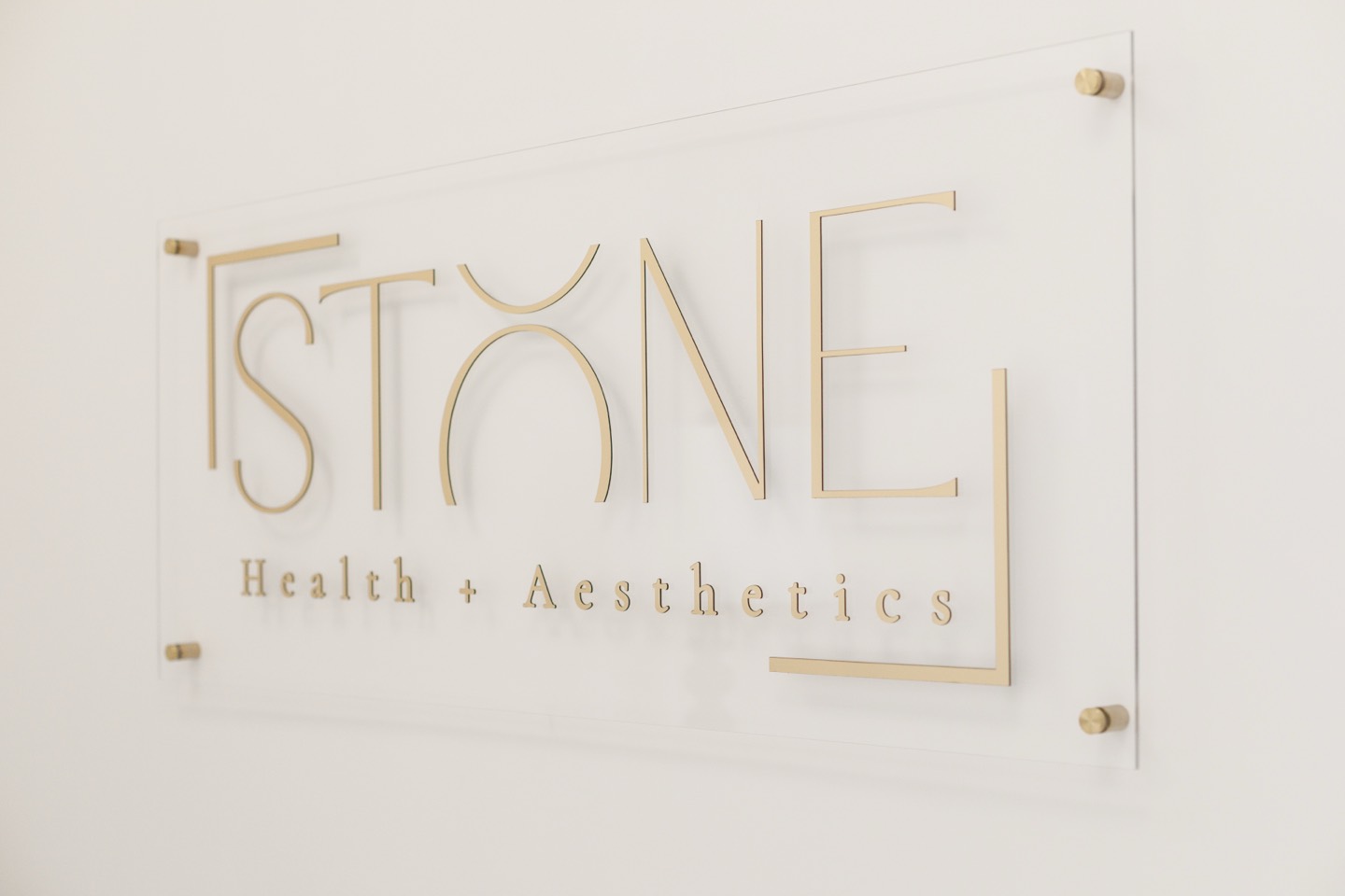 The Stone Health + Aesthetics sign in gold lettering on a clear acrylic panel