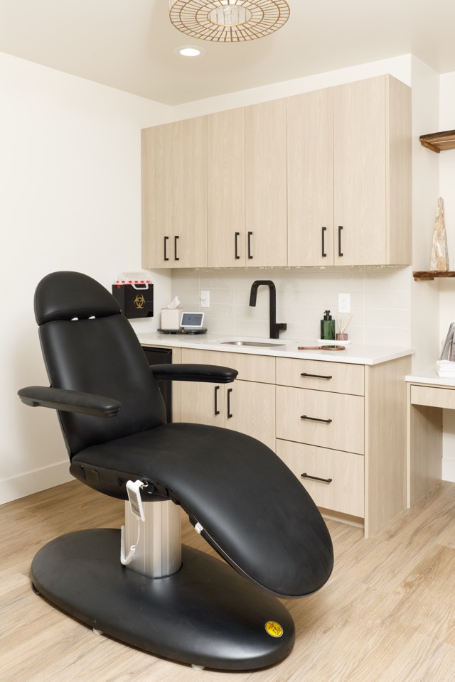 A black treatment chair beside light wood cabinetry in a treatment room