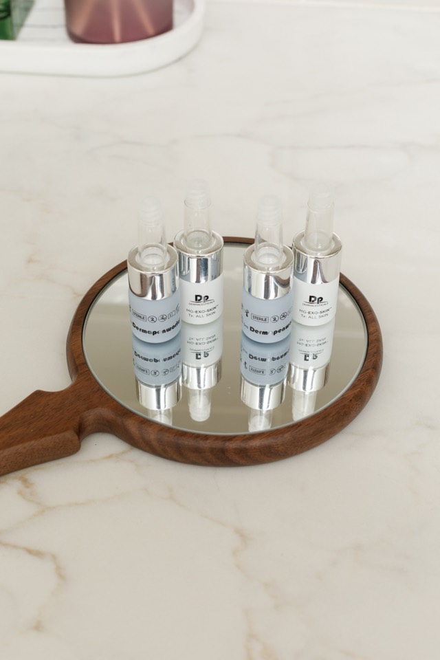 Skincare vials arranged on a wooden hand mirror on a marble counter