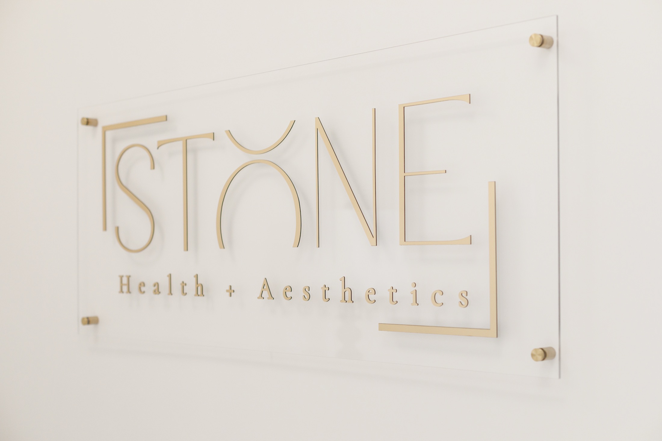 The Stone Health + Aesthetics sign in gold lettering on a clear acrylic panel