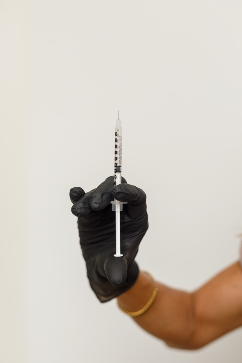 A gloved hand holding a syringe against a soft neutral wall
