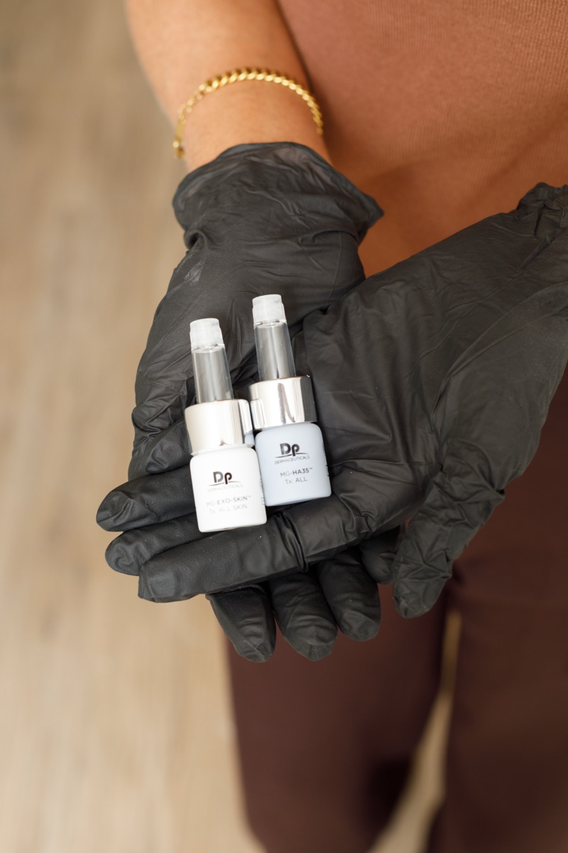 Gloved hands holding two small bottles of Dermaceuticals skincare